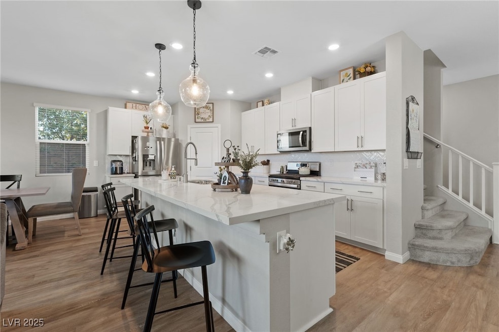 Kitchen featuring decorative backsplash, white cabinetry, appliances with stainless steel finishes, light wood-style floors, and a breakfast bar