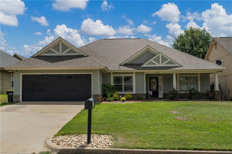 Craftsman-style house featuring roof with shingles, a garage, a front yard, stone siding, and driveway