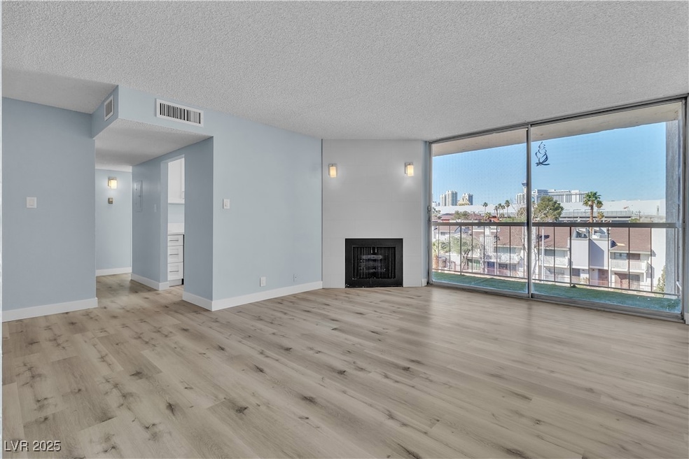 Unfurnished living room with a textured ceiling, wood finished floors, floor to ceiling windows, a view of city, and a fireplace
