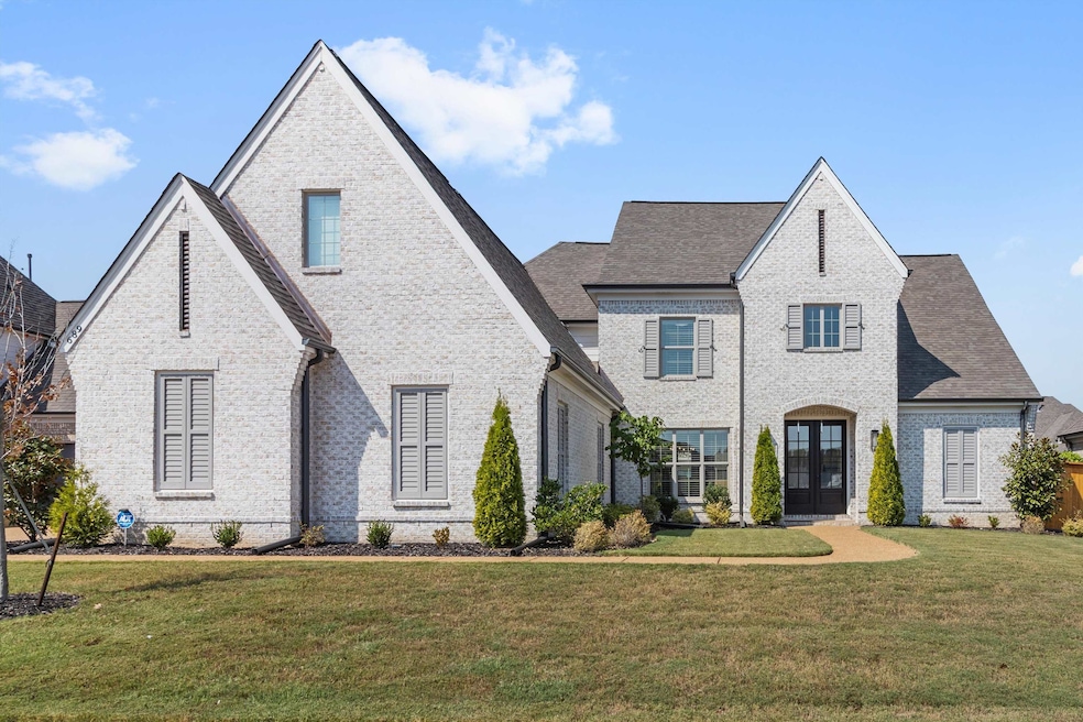 French country style house with brick siding, a front yard, roof with shingles, and french doors