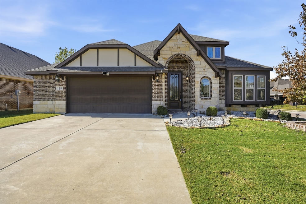 Tudor-style house featuring stone siding, a front yard, driveway, an attached garage, and brick siding