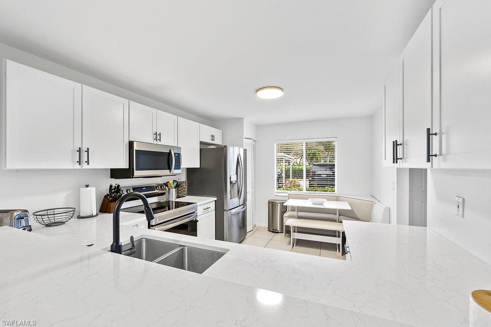Kitchen featuring white cabinets, light stone countertops, stainless steel appliances, a sink, and light tile patterned flooring