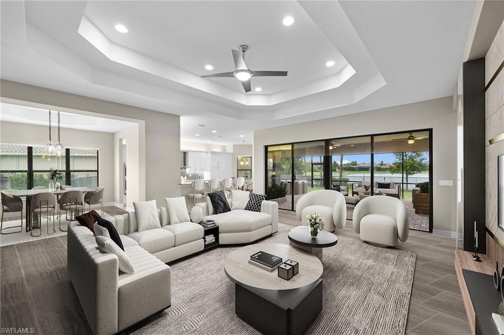 Living room with ceiling fan, a raised ceiling, recessed lighting, baseboards, and a chandelier