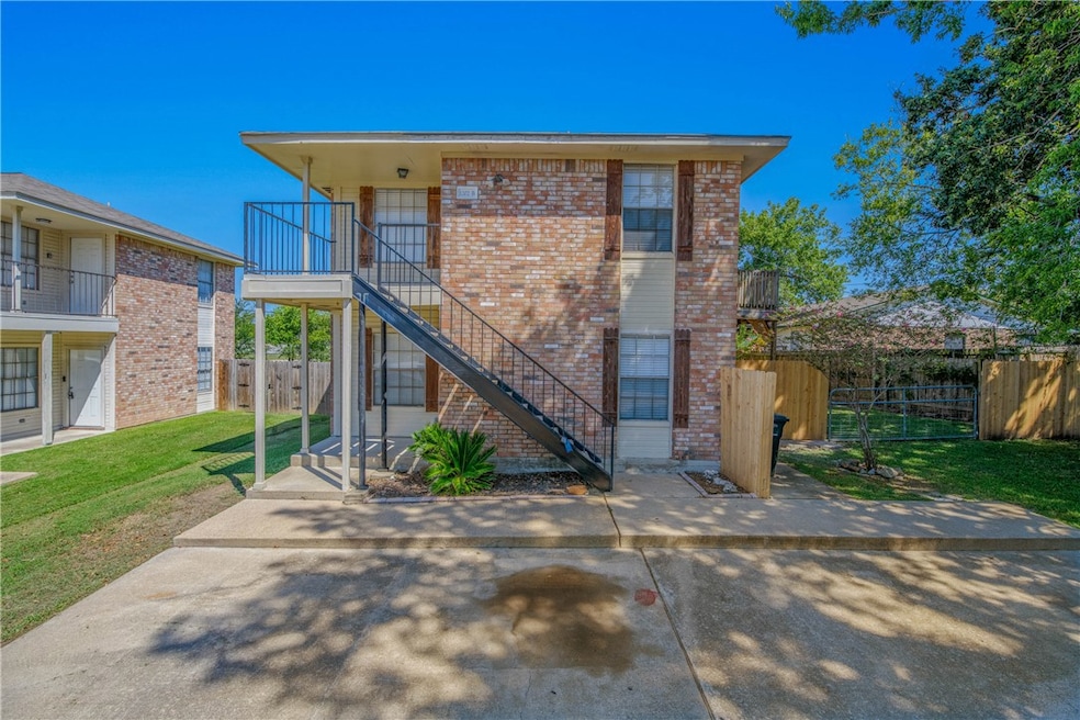 View of front of property featuring brick siding, stairway, a balcony, and a patio area