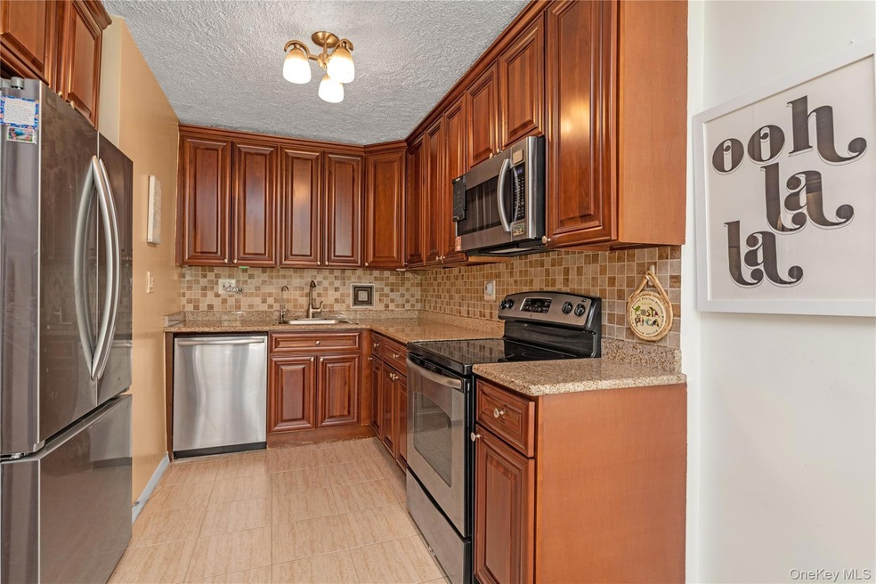 Kitchen with appliances with stainless steel finishes, light stone counters, backsplash, brown cabinets, and a textured ceiling