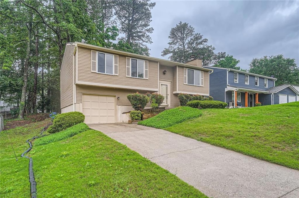 Split foyer home with a chimney, an attached garage, driveway, and a front lawn