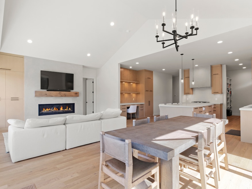 Dining space with light wood-type flooring, recessed lighting, a glass covered fireplace, a chandelier, and high vaulted ceiling