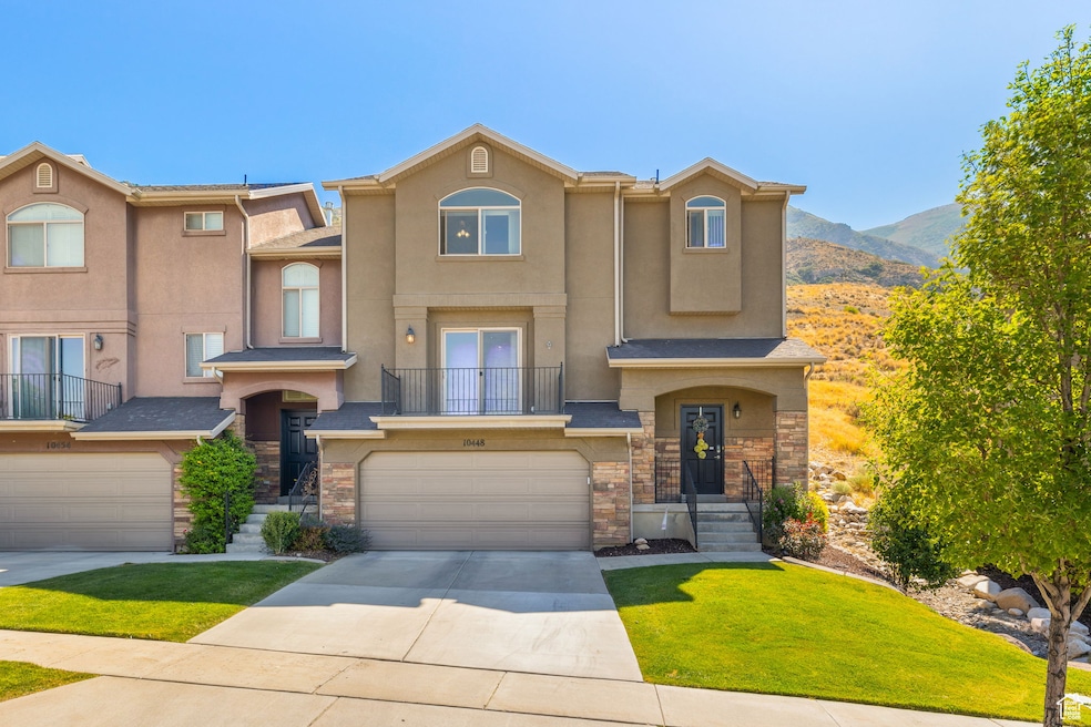 View of front facade featuring stone siding, an attached garage, driveway, and a balcony