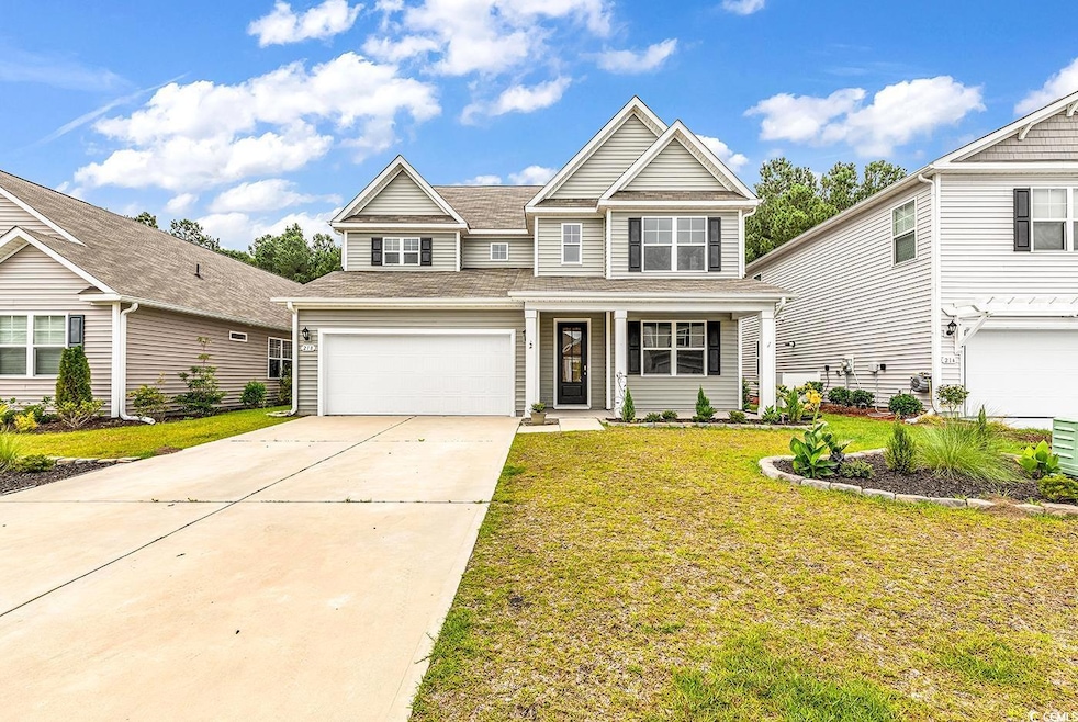Traditional-style house featuring a shingled roof, covered porch, an attached garage, driveway, and a front yard