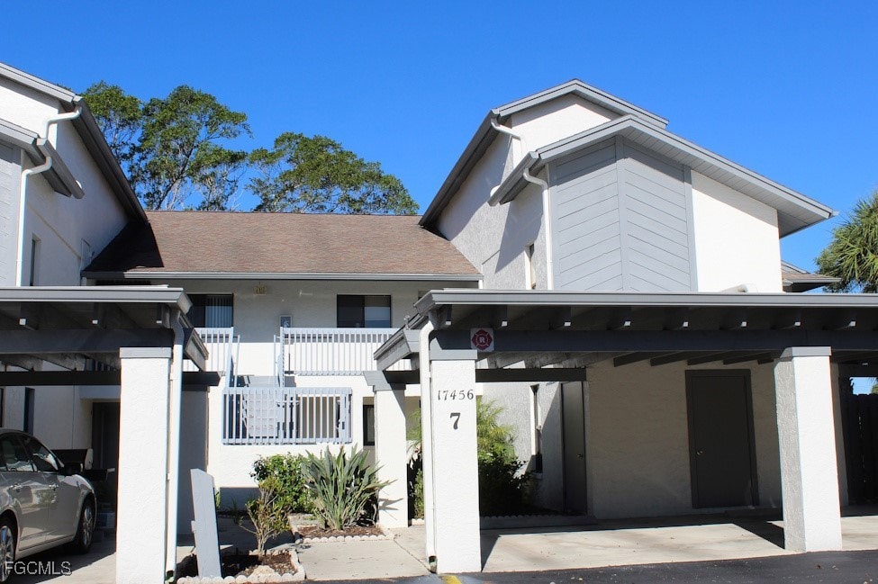 View of front facade featuring stucco siding, covered parking, and roof with shingles