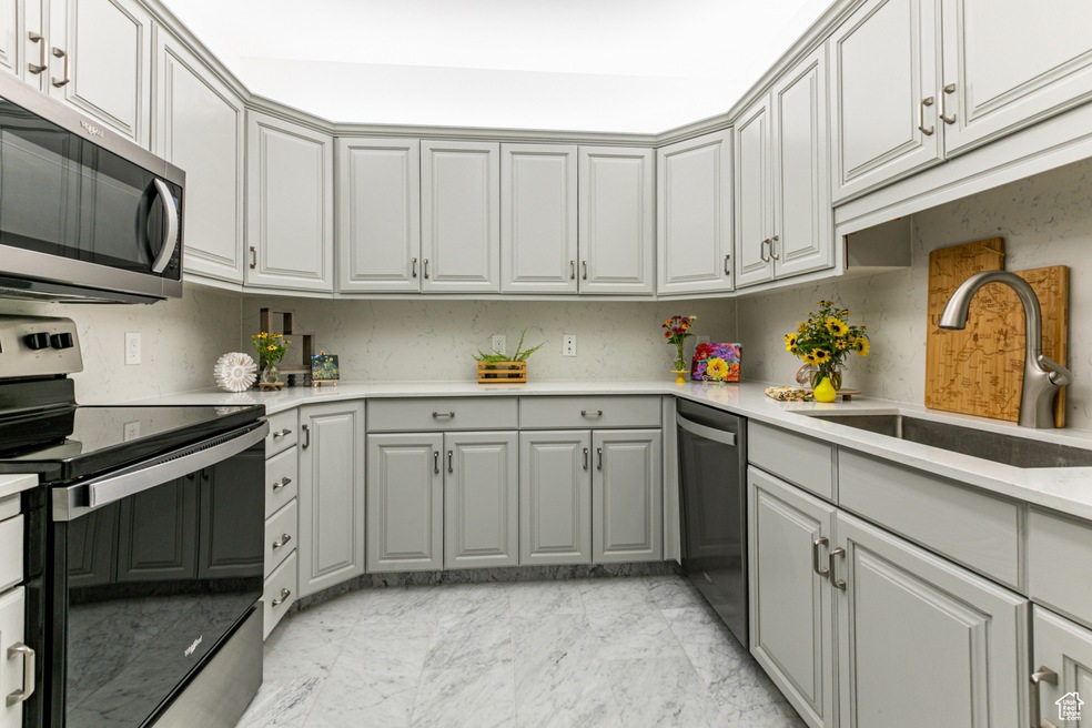 Kitchen featuring stainless steel appliances, gray cabinetry, light marble finish flooring, and light countertops