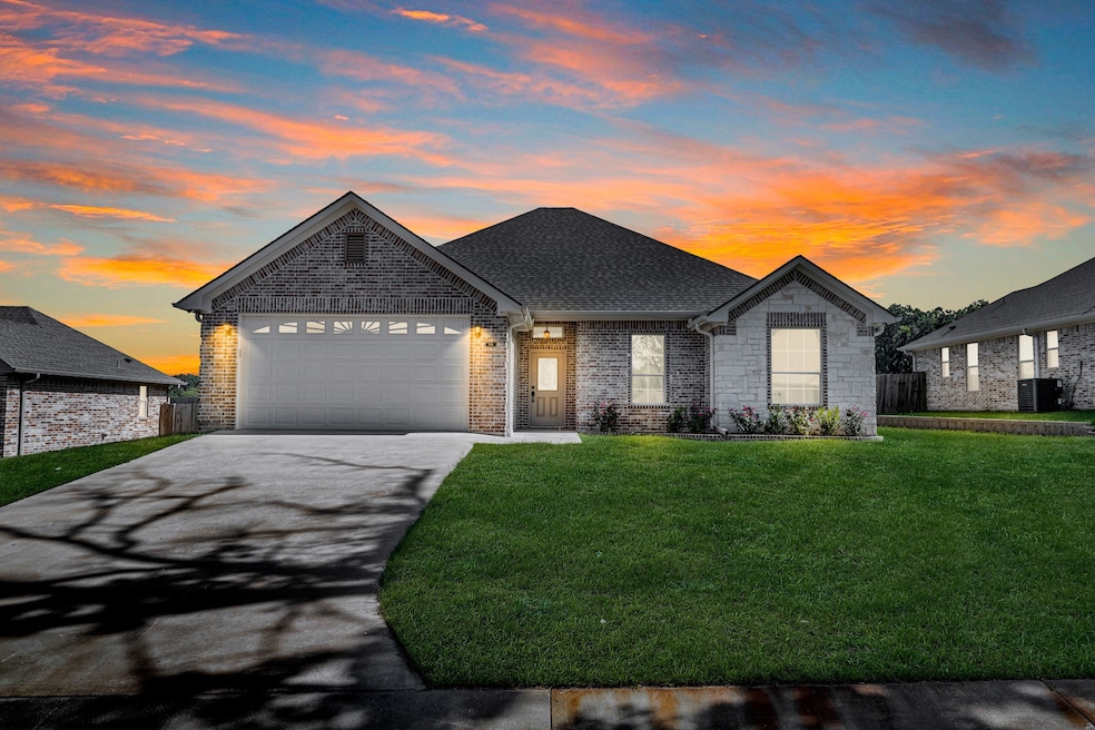 View of front of house featuring a lawn, driveway, a shingled roof, an attached garage, and brick siding