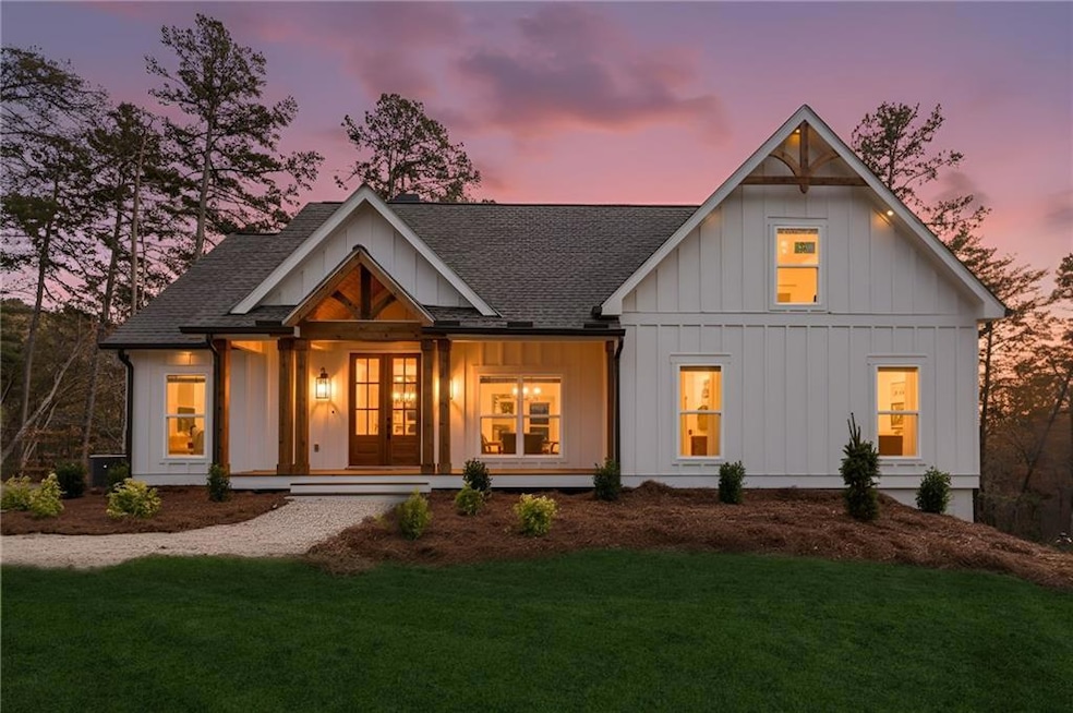 Front of property at dusk with board and batten siding, roof with shingles, a porch, and a yard