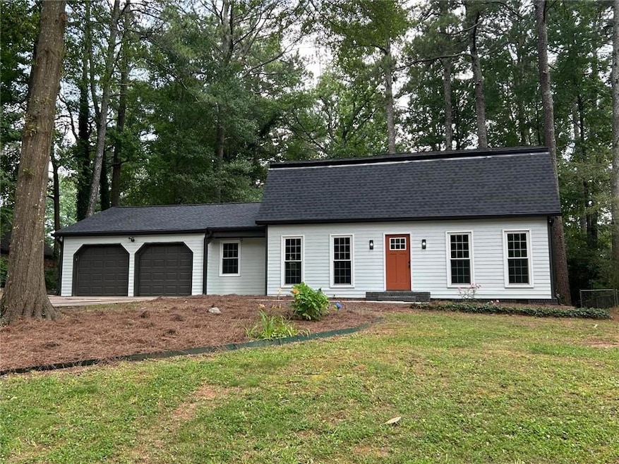 View of front of home with a garage, a front yard, roof with shingles, and view of scattered trees