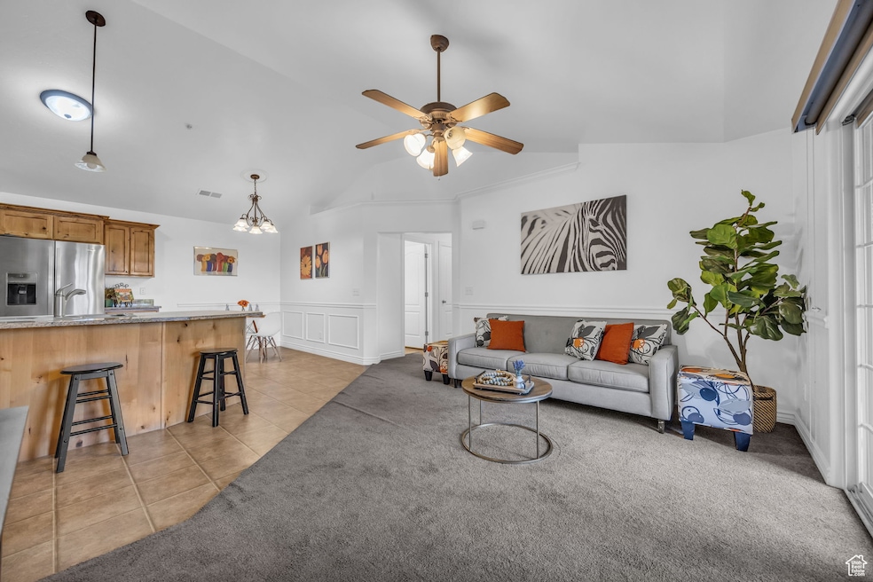 Living area featuring vaulted ceiling, light tile patterned floors, a ceiling fan, light carpet, and a wainscoted wall