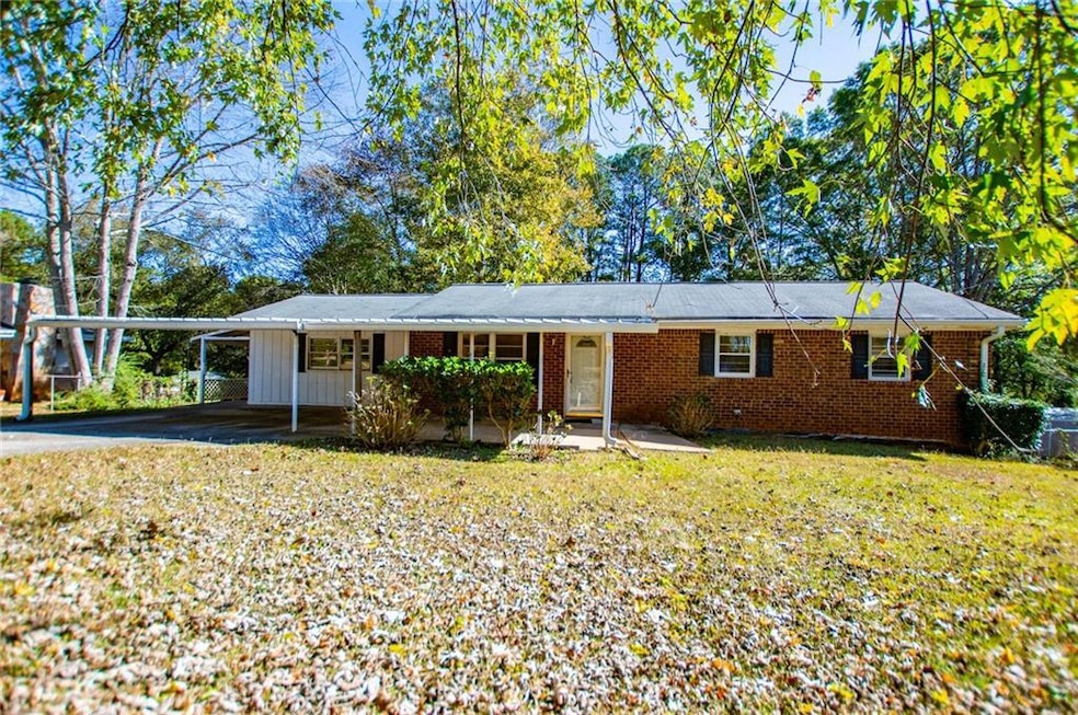 Ranch-style house featuring a carport, brick siding, a front yard, driveway, and board and batten siding