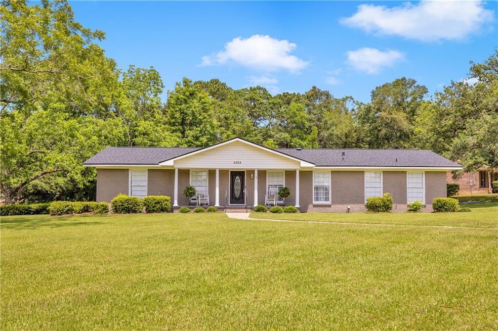 Ranch-style home with covered porch, a front lawn, and view of scattered trees