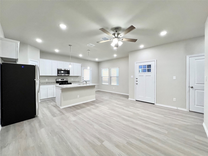 Kitchen featuring stainless steel appliances, decorative light fixtures, light wood-type flooring, a center island with sink, and open floor plan