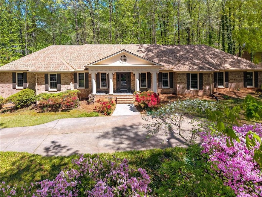 Ranch-style home featuring brick siding, a view of trees, and covered porch