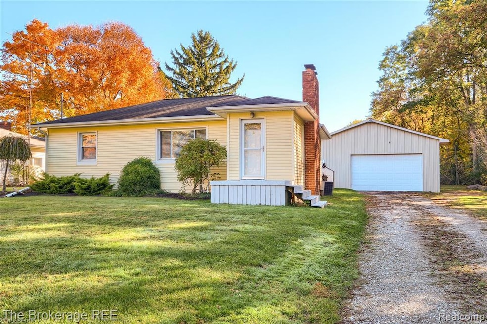View of front of property with an outbuilding, a chimney, a front yard, and a detached garage