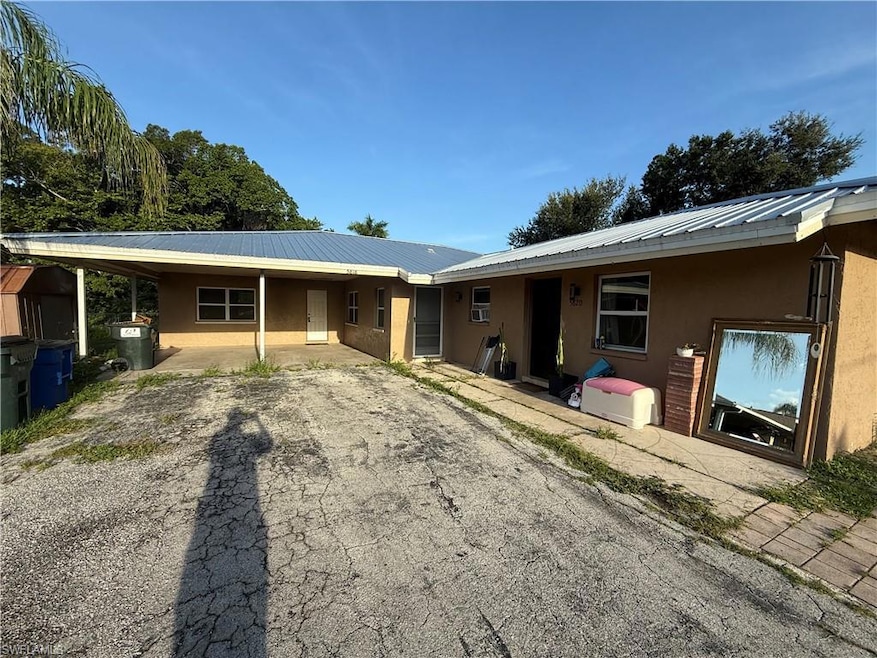 Back of property with stucco siding, a metal roof, driveway, and cooling unit