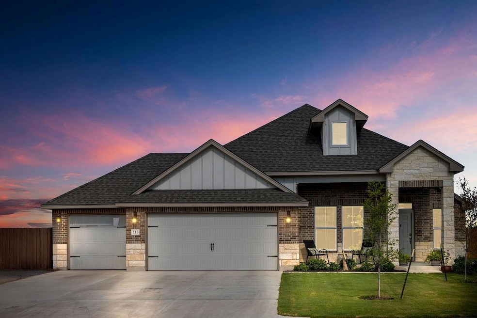 View of front of home with stone siding, roof with shingles, a garage, and brick siding