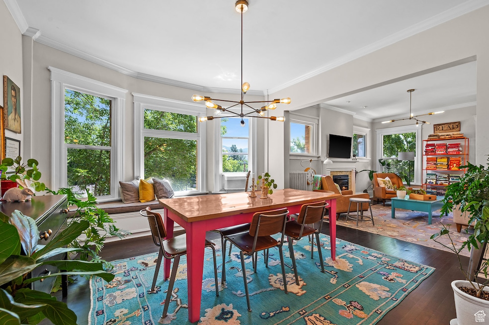 Dining room featuring crown molding, a glass covered fireplace, dark wood-style flooring, and a chandelier