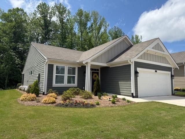 View of front of house featuring board and batten siding, an attached garage, concrete driveway, a front lawn, and roof with shingles