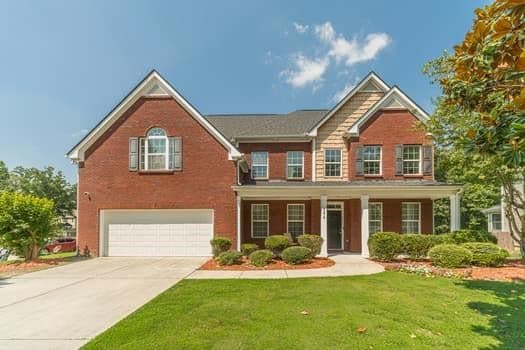 View of front of house with a garage, a front yard, driveway, brick siding, and covered porch