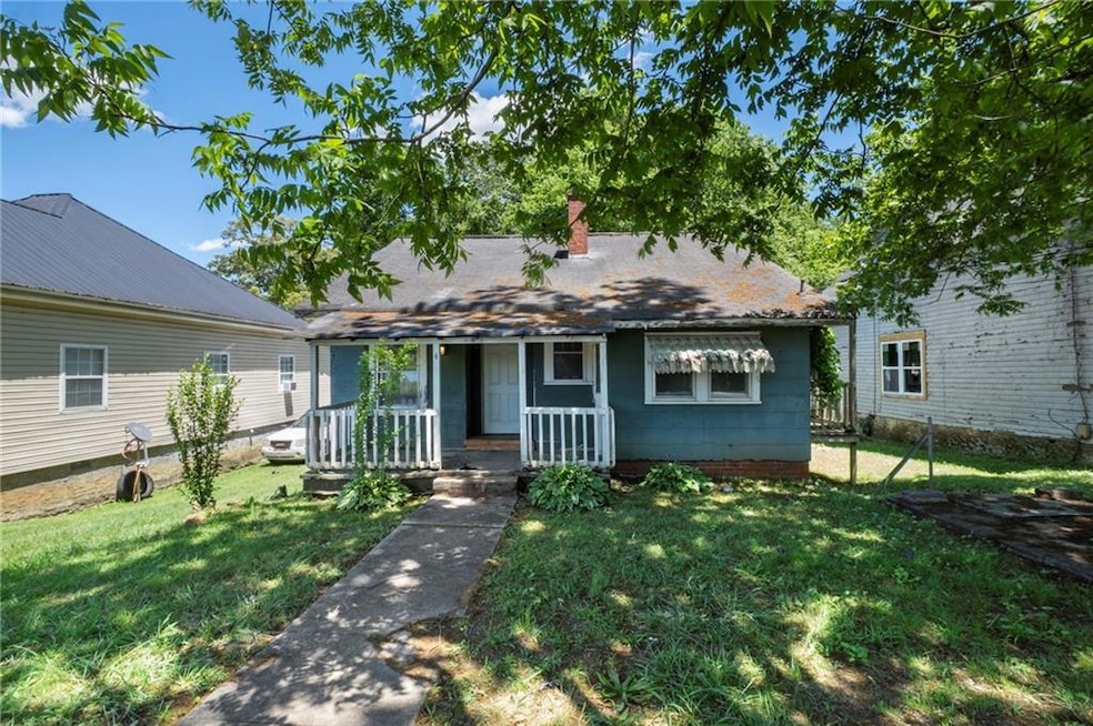 View of front of home with covered porch, a front yard, and a chimney
