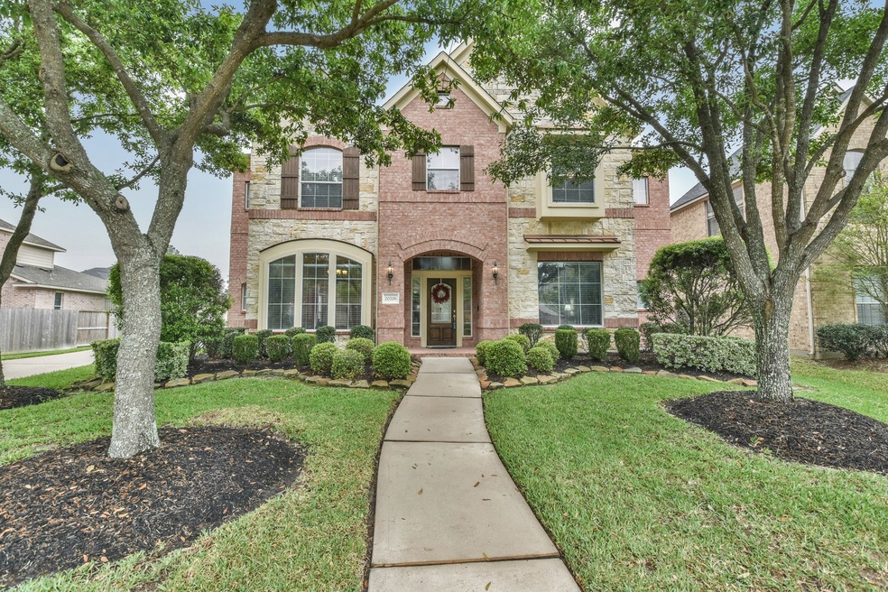 Beautiful curb appeal with brick, stone, shutters, professional landscaping, and shade trees