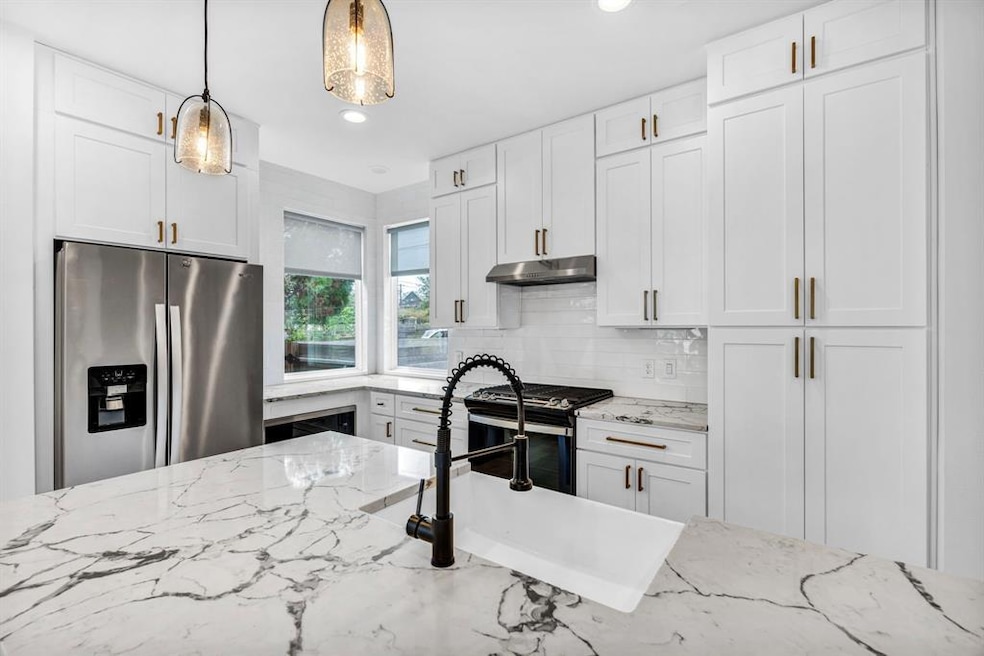 Kitchen with stainless steel appliances, white cabinets, light stone counters, backsplash, and hanging light fixtures