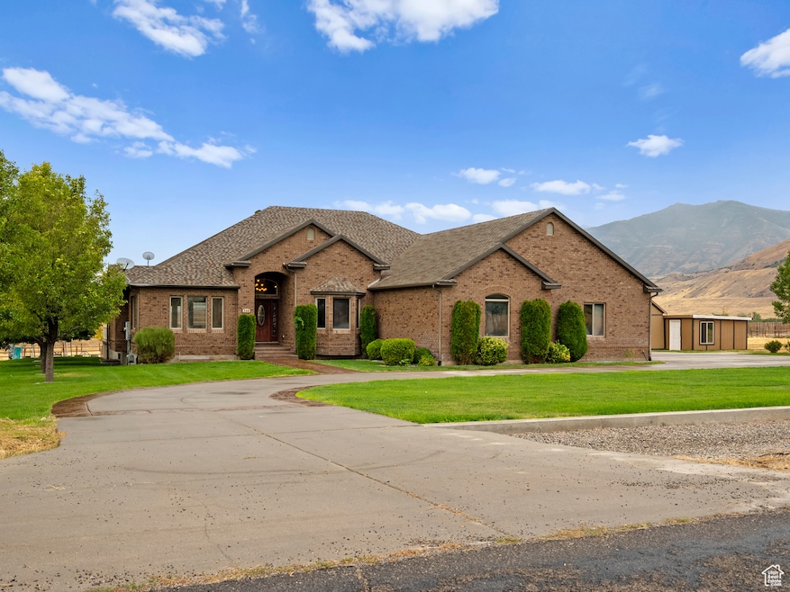 Ranch-style home featuring curved driveway, brick siding, a front yard, a mountain view, and roof with shingles