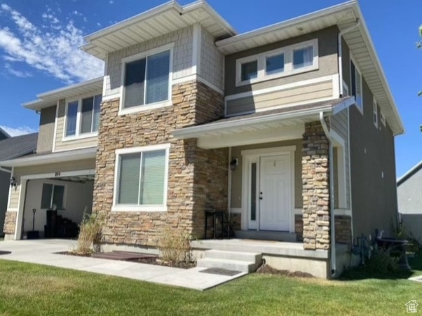 View of front of house featuring stone siding, a front yard, and a garage