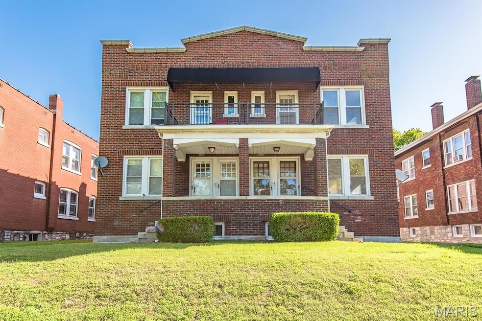 View of front of property with brick siding, a front yard, and a balcony