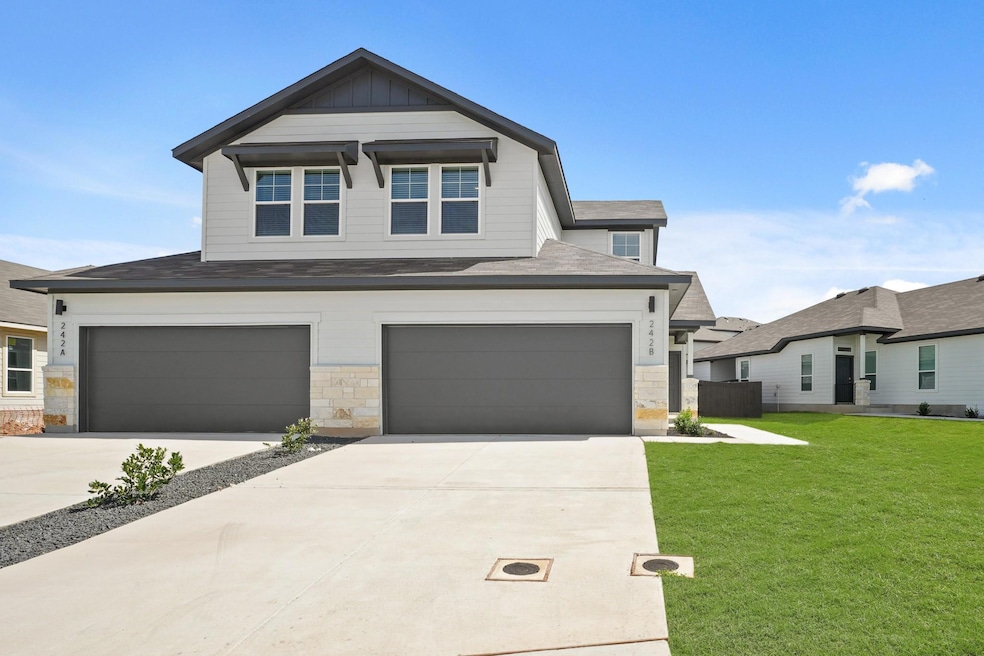 View of front of house with a front lawn, driveway, a garage, board and batten siding, and stone siding