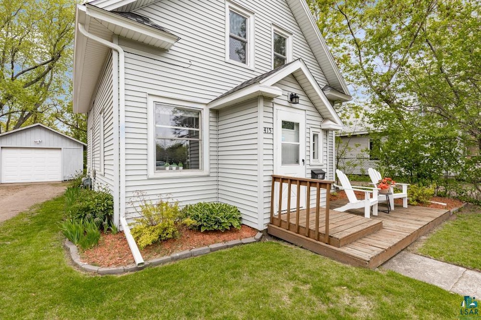 View of front of house featuring a deck, a detached garage, an outbuilding, and a front yard
