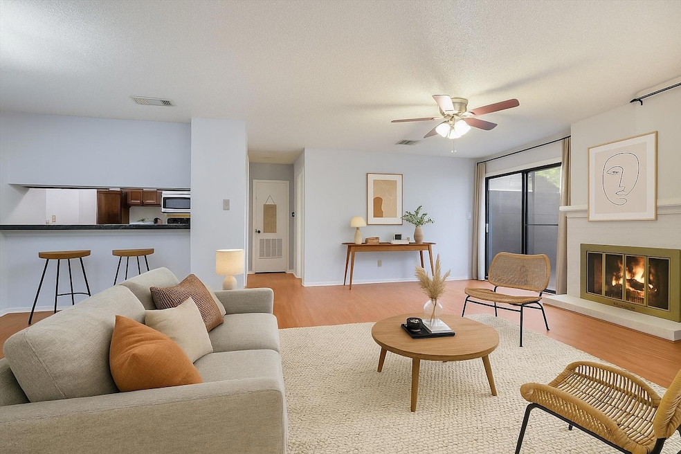 Living area with light wood-type flooring, a ceiling fan, and a glass covered fireplace