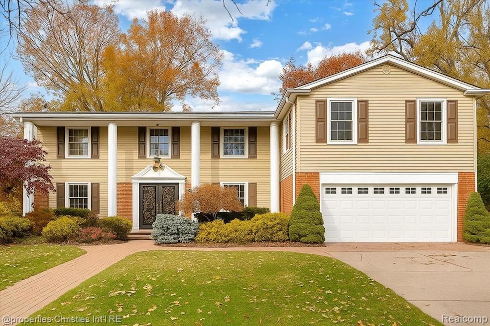 Greek revival house with an attached garage, driveway, a front yard, and brick siding