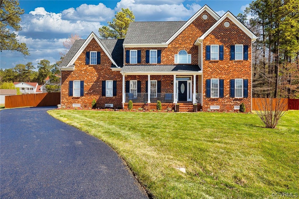 The house for sale has both brick and vinyl siding, is situated on a cul-de-sac lot, and features a beautifully manicured yard with lush landscaping and colorful flower beds.