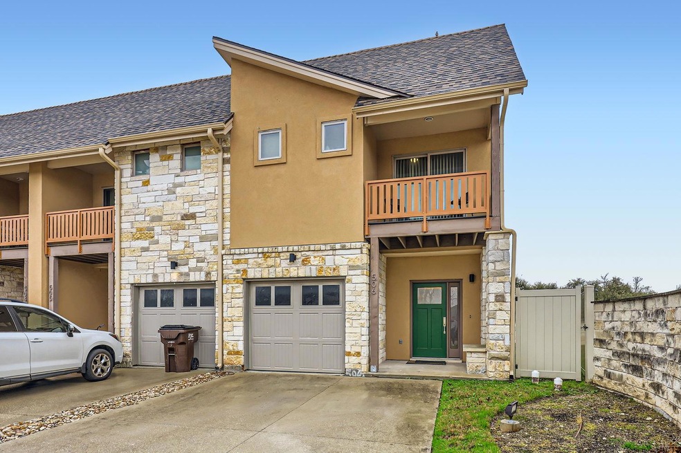 Townhome / multi-family property with a balcony, stone siding, driveway, an attached garage, and stucco siding