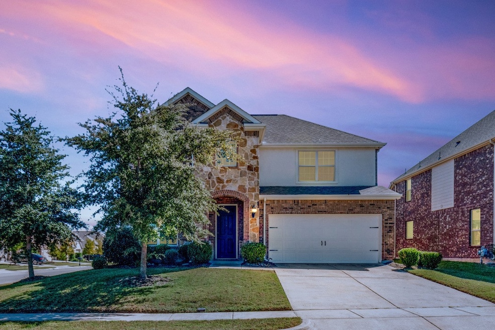 Traditional home featuring a front yard, driveway, a garage, stucco siding, and stone siding