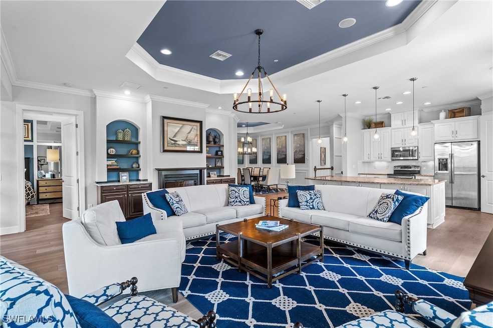 Living area featuring a raised ceiling, light wood-type flooring, crown molding, a chandelier, and recessed lighting