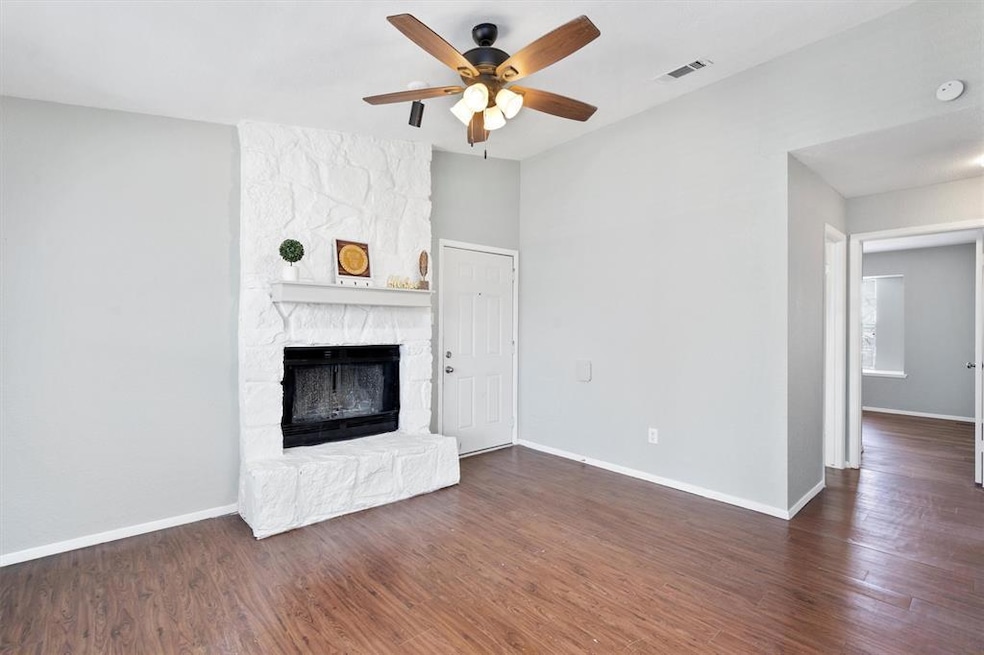 Unfurnished living room featuring dark wood finished floors, a stone fireplace, and a ceiling fan