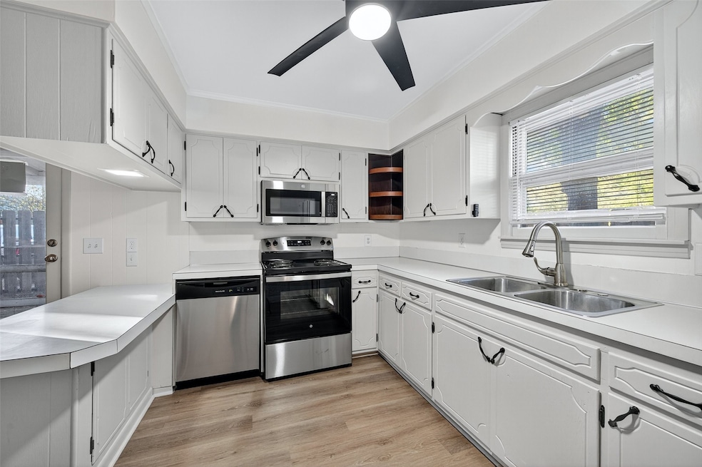 Kitchen with healthy amount of natural light, appliances with stainless steel finishes, light countertops, light wood-style flooring, and ornamental molding