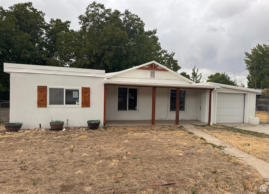 View of front of home with covered porch, a garage, driveway, and stucco siding