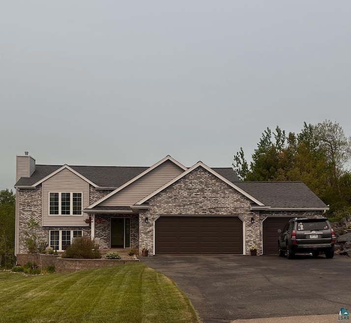 View of front facade featuring an attached garage, asphalt driveway, a front lawn, a chimney, and a shingled roof