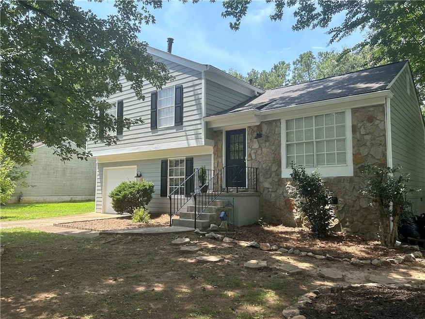 Tri-level home featuring stone siding, an attached garage, and driveway