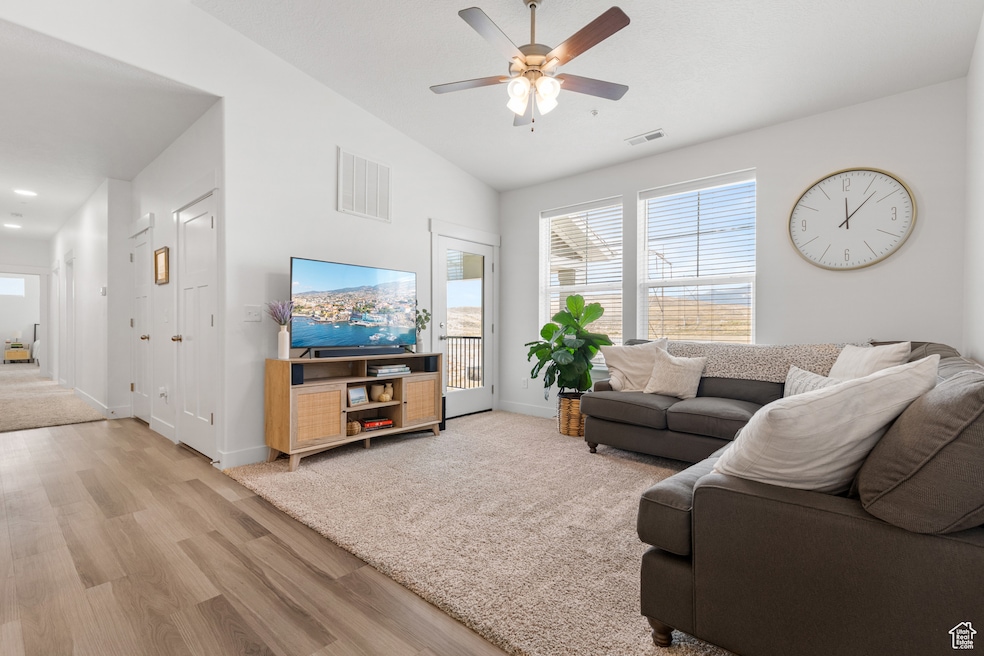 Living room featuring lofted ceiling, healthy amount of natural light, light wood finished floors, and a ceiling fan