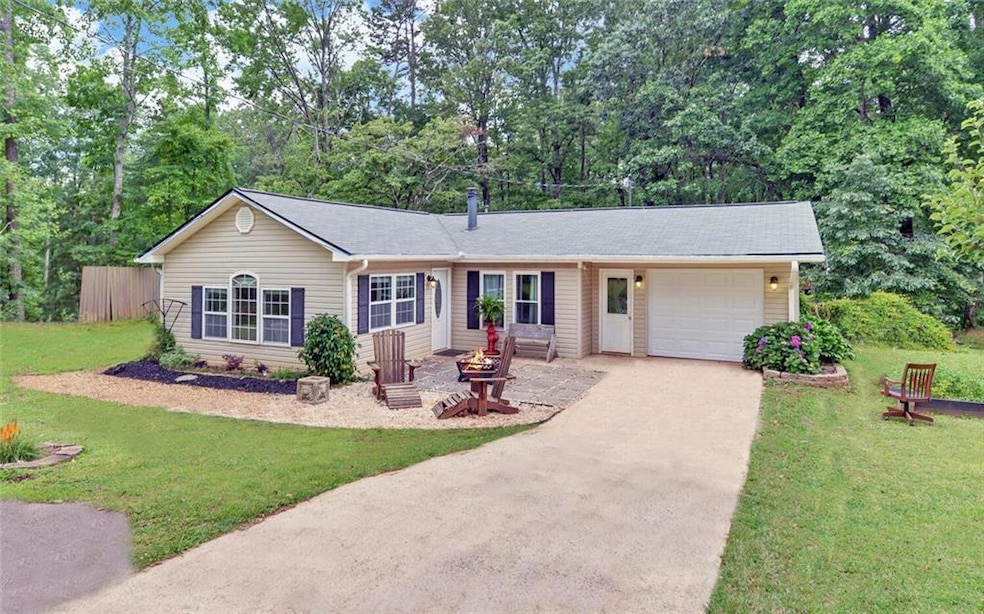 Single story home with an attached garage, concrete driveway, a front yard, and view of wooded area